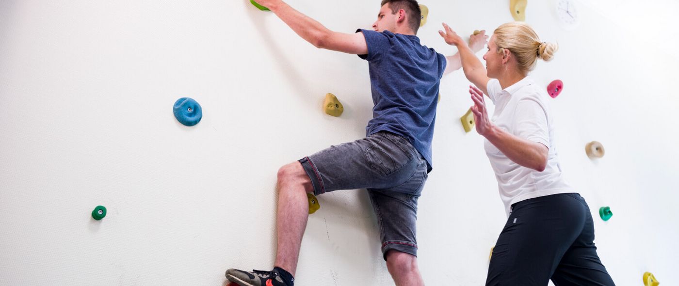 Therapeut unterstützt Patient an der Kletterwand