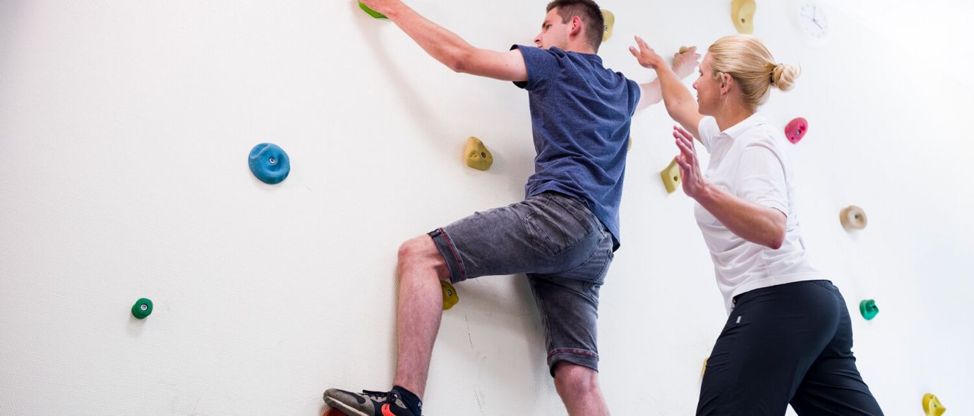Therapeut unterstützt Patient an der Kletterwand