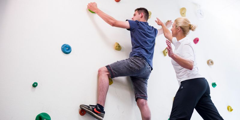 Therapeut unterstützt Patient an der Kletterwand
