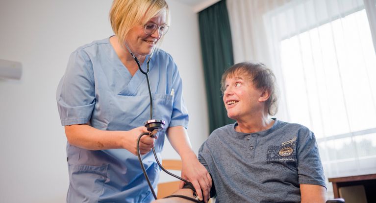 Pflegekraft misst Blutdruck bei einem Patienten im Rollstuhl