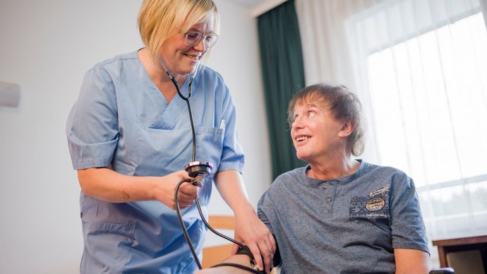 Pflegekraft misst Blutdruck bei einem Patienten im Rollstuhl